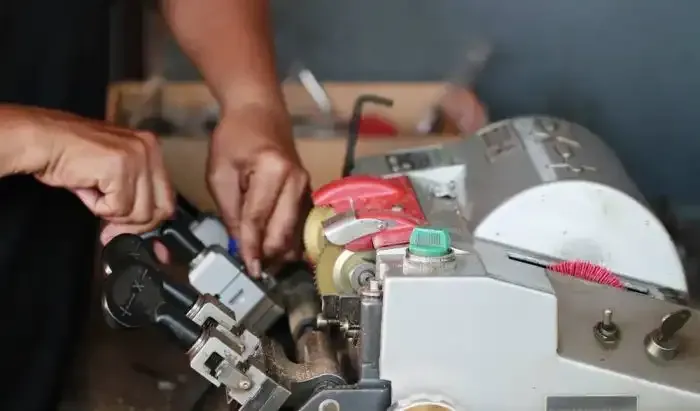Hands adjusting a compact machine with tools and red and white parts in a workshop