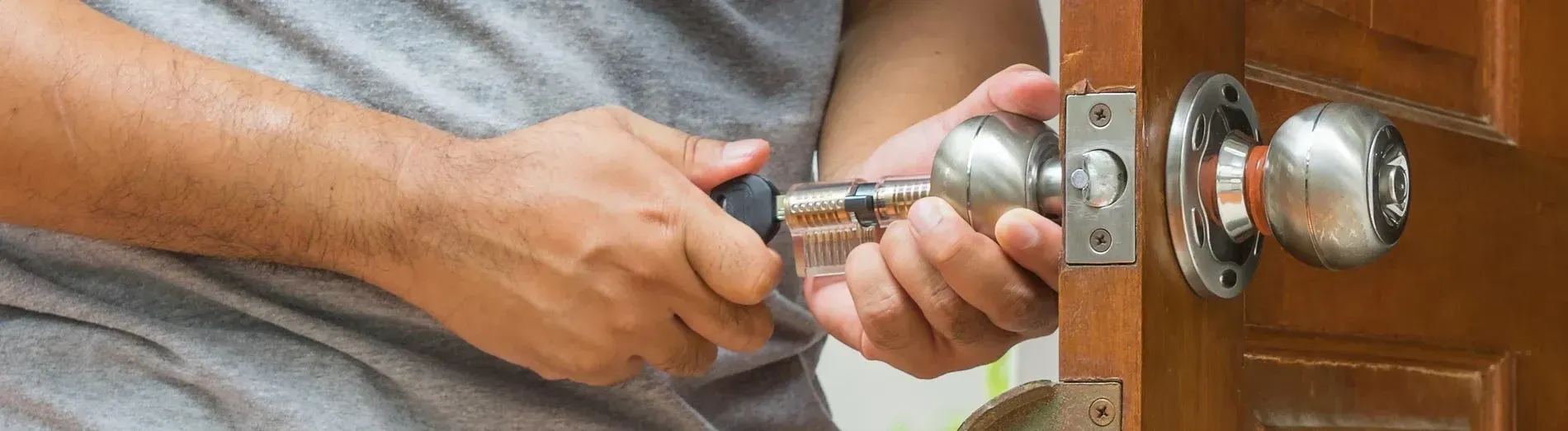 Person installing a silver doorknob on a wooden door with a screwdriver