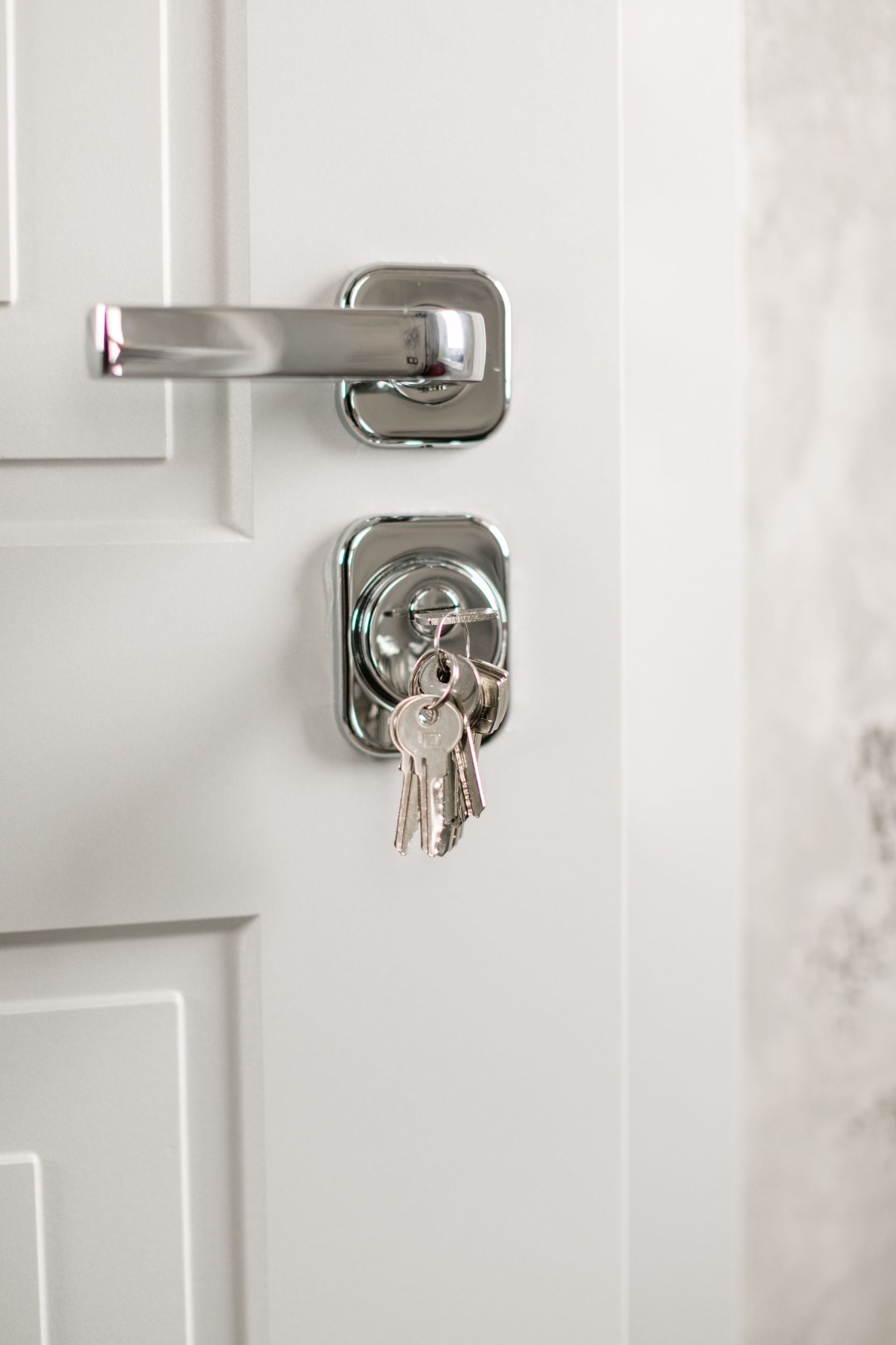 Chrome door lock with keys hanging in the keyhole on a white door