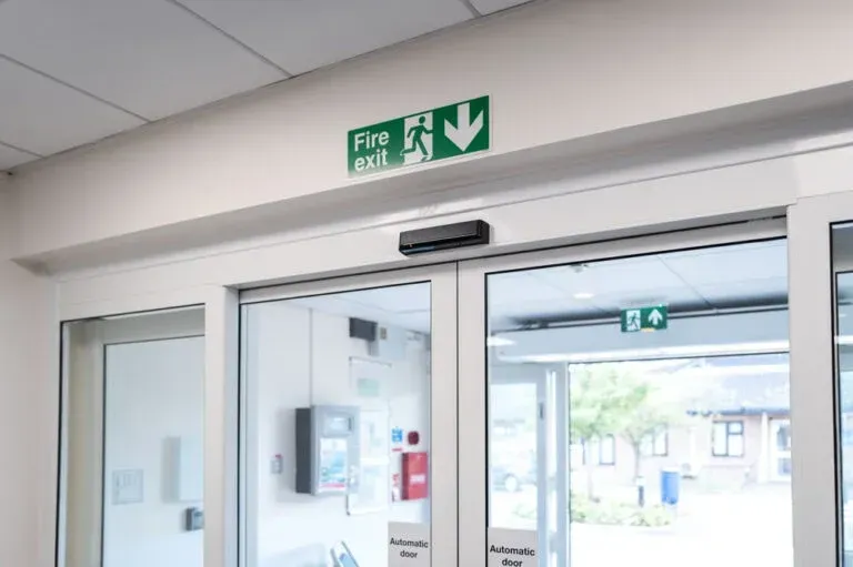 Building entrance with glass doors and a green fire exit sign above them