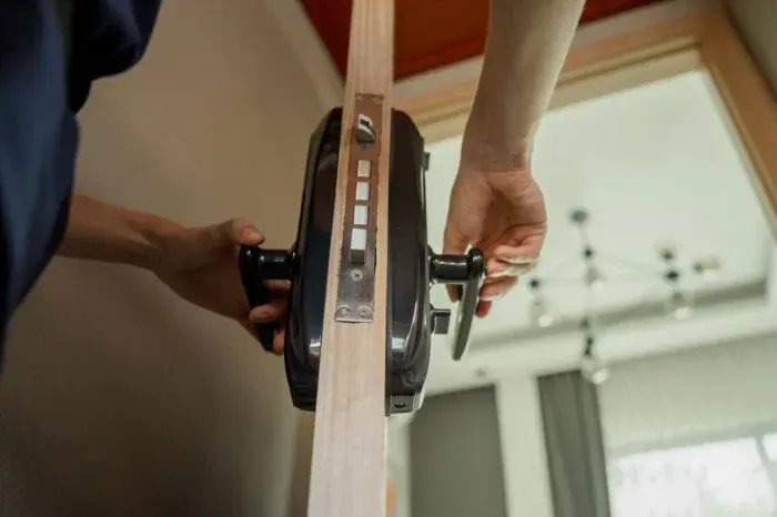 Hands installing a door lock on a wooden door, with a screwdriver and black hardware.