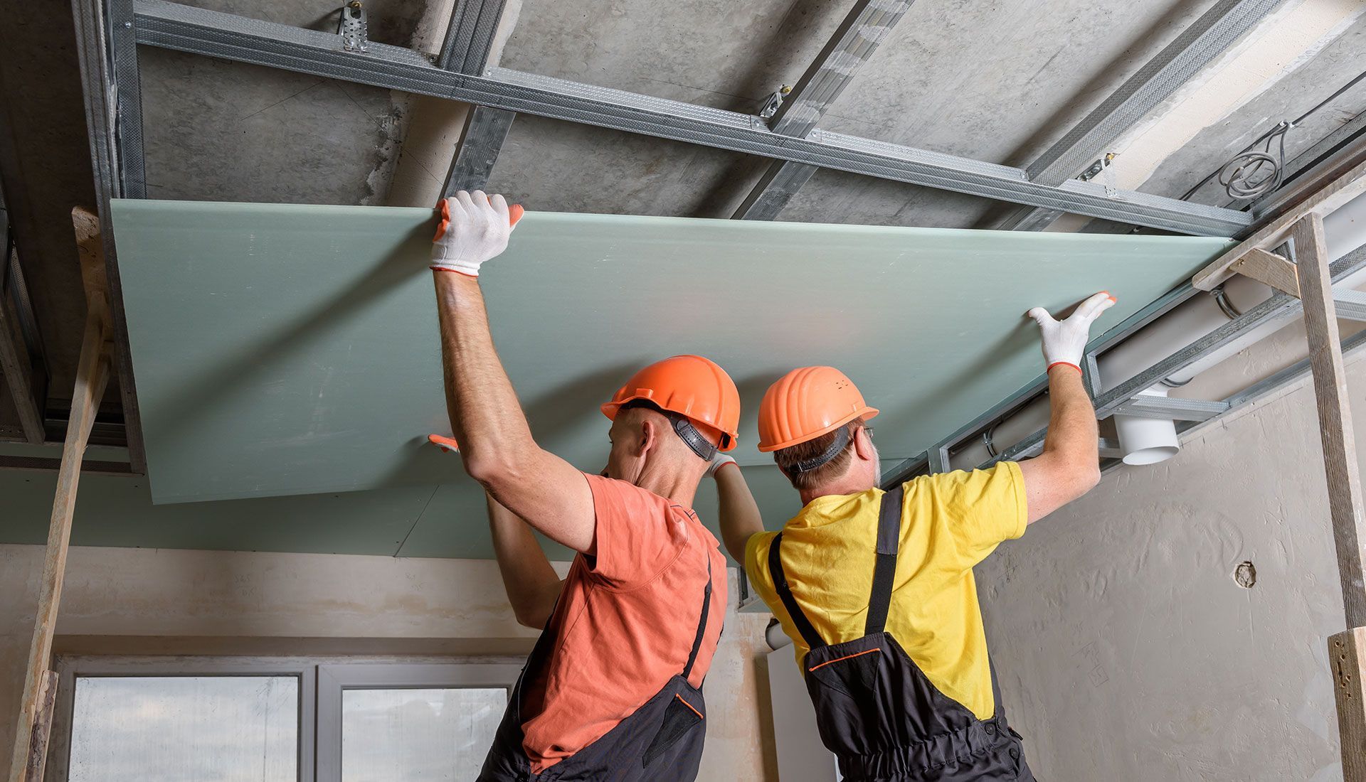 Two men are hanging a piece of drywall from the ceiling.