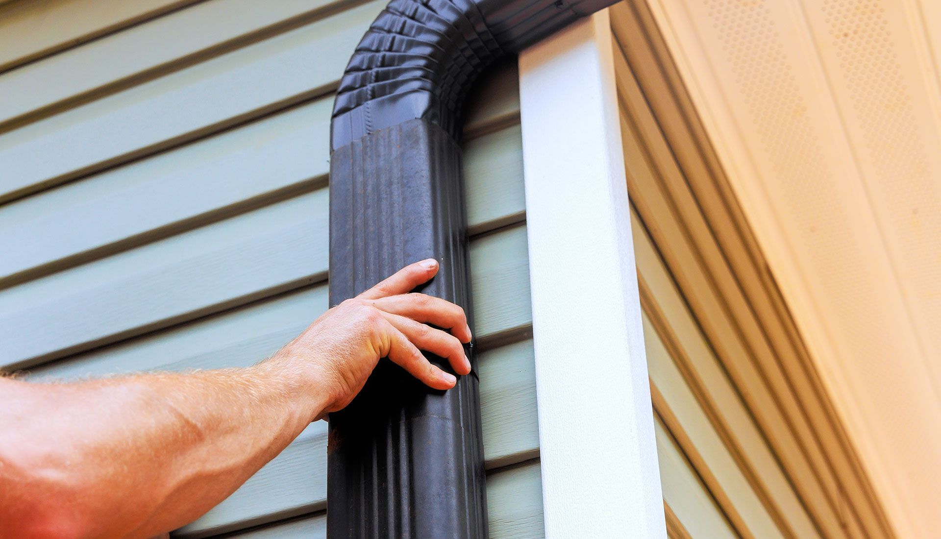 A man is fixing a gutter on the side of a house.
