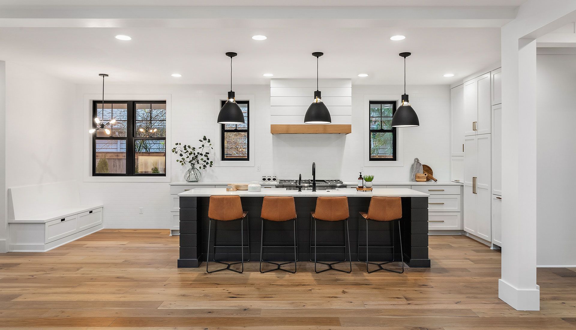A kitchen with a large island , wooden floors , and white cabinets.