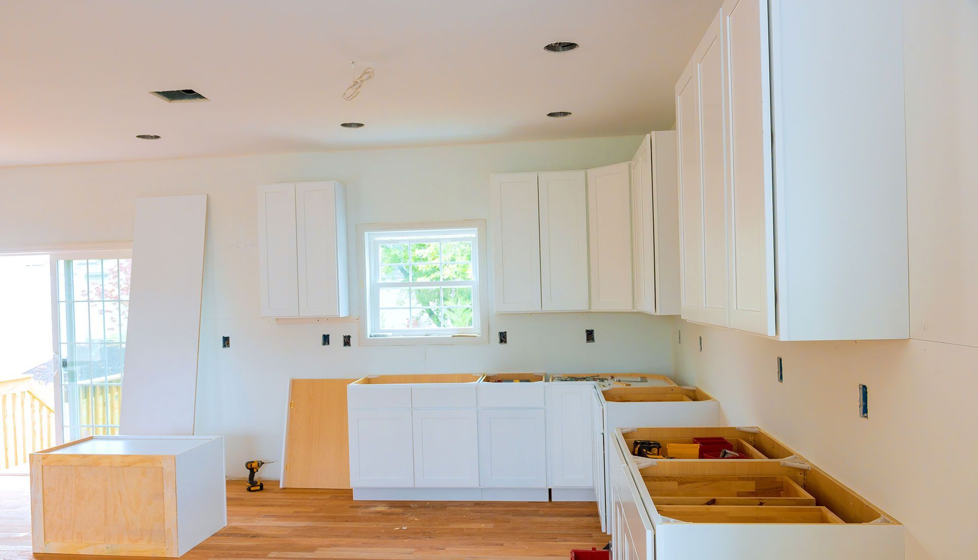 A kitchen under construction with white cabinets and wooden floors.