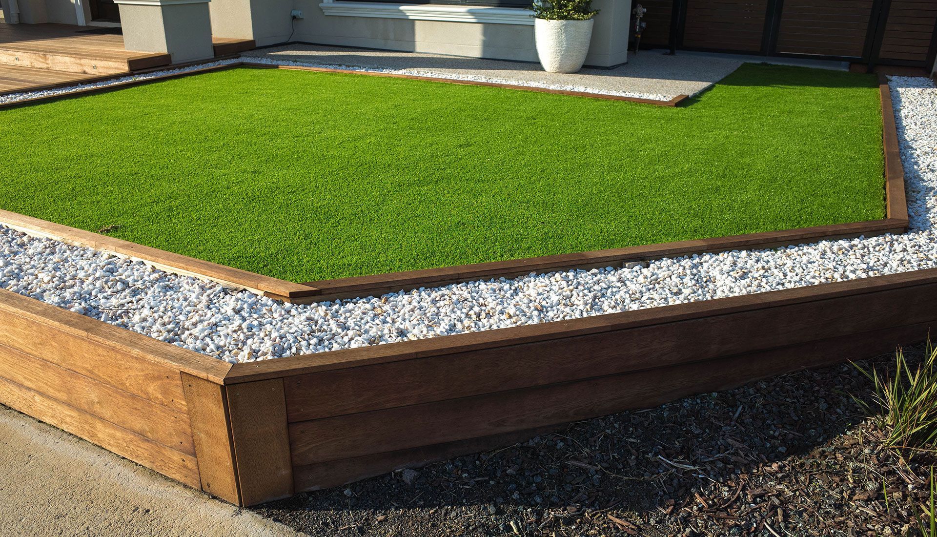 A lawn with a wooden border and gravel in front of a house.