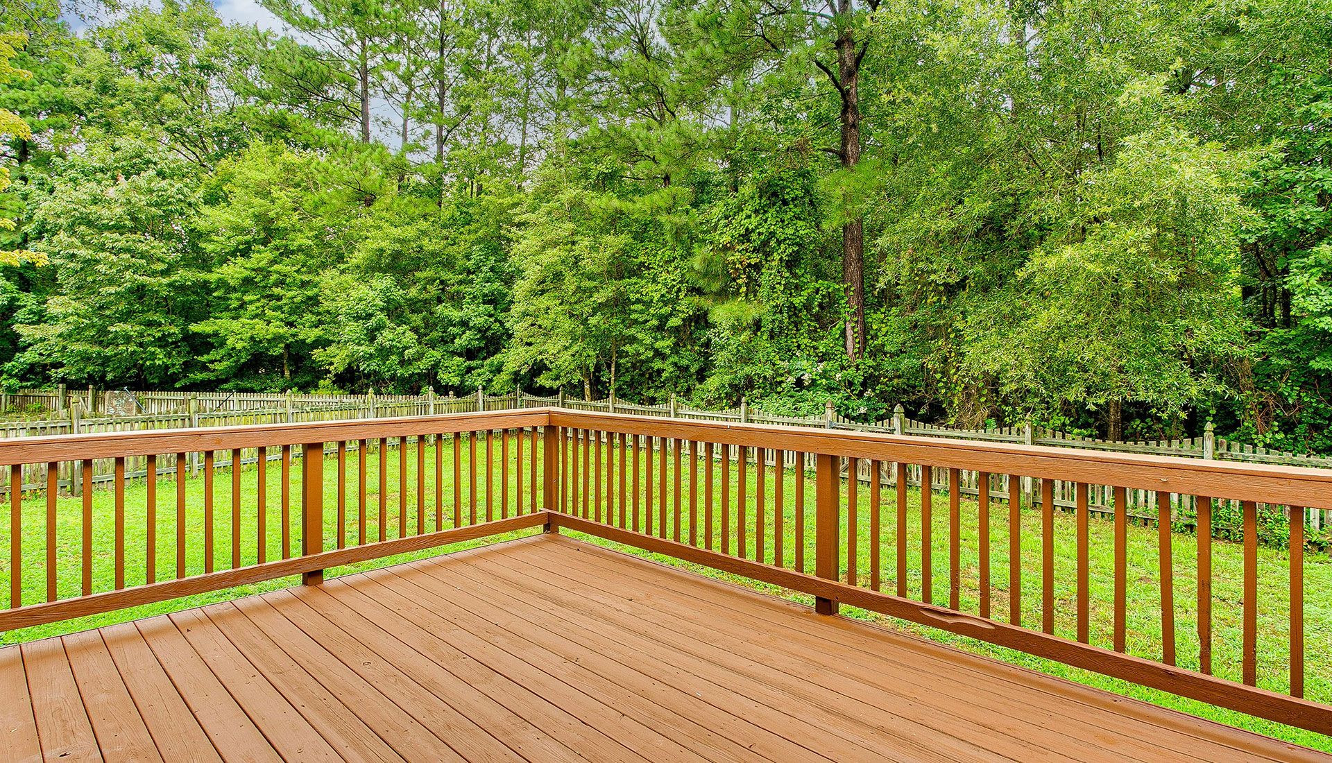 An empty wooden deck with a wooden railing and trees in the background.
