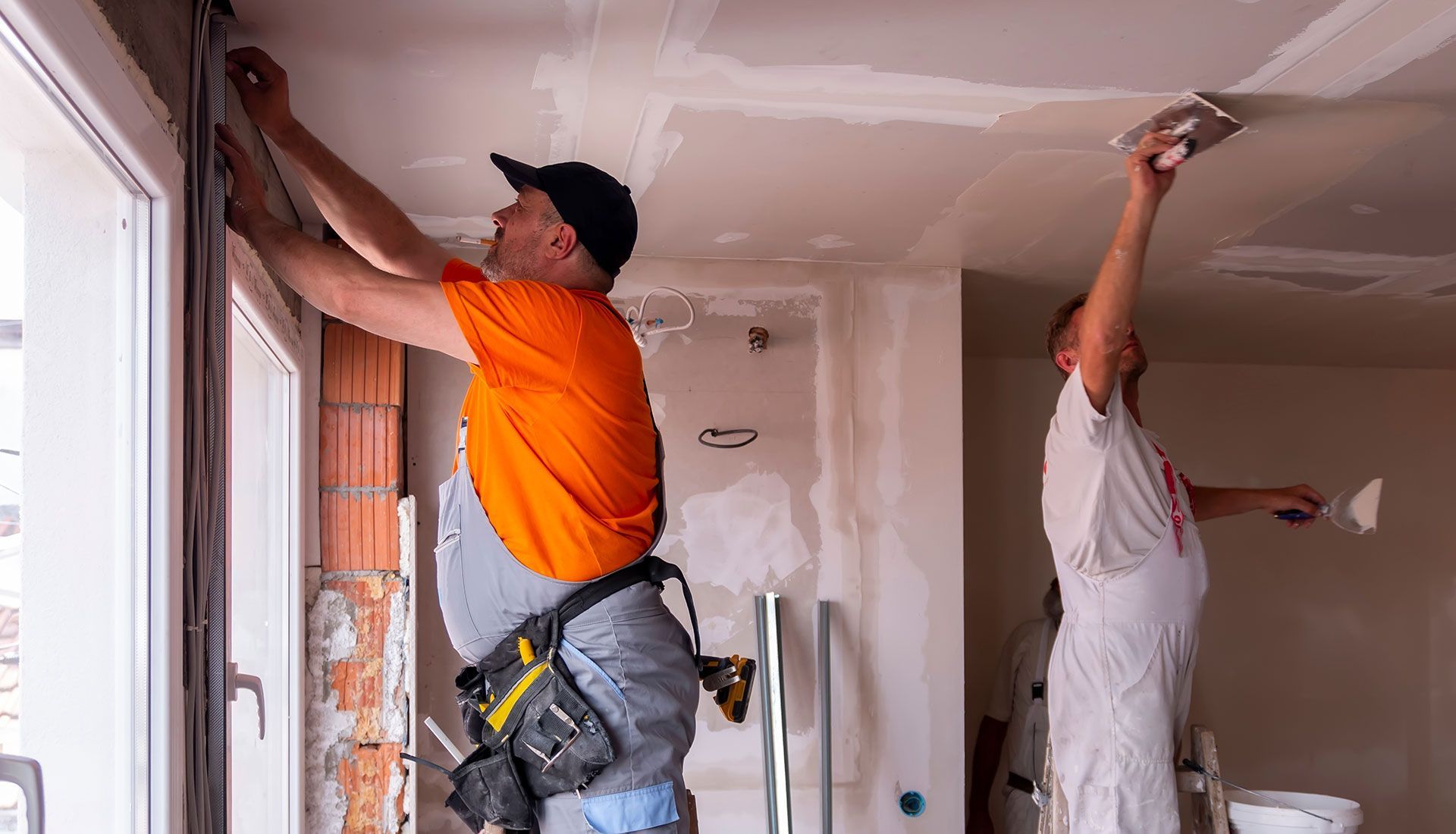 Two men are working on a ceiling in a room.