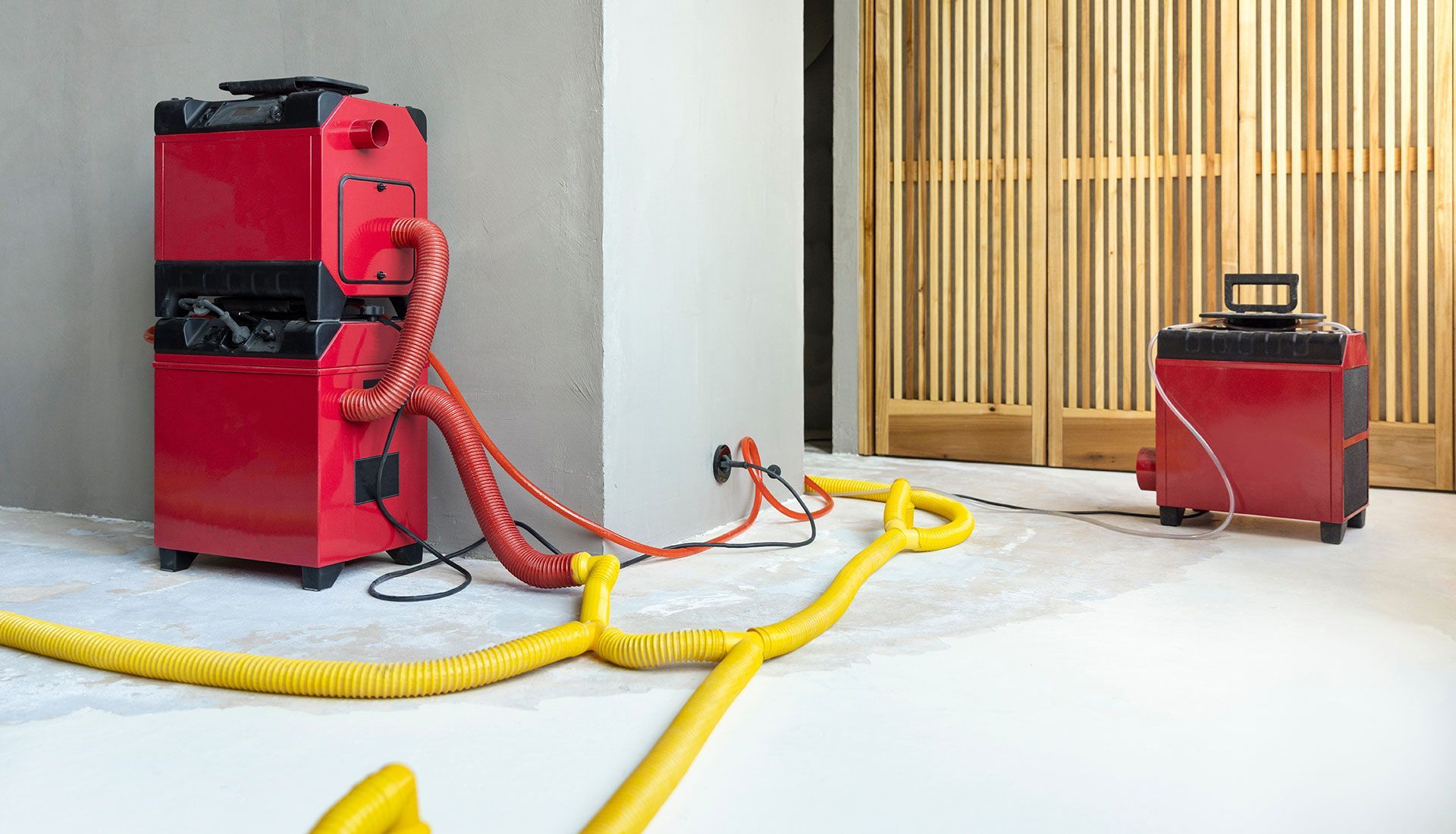 A red dryer is sitting next to a yellow hose in a room.