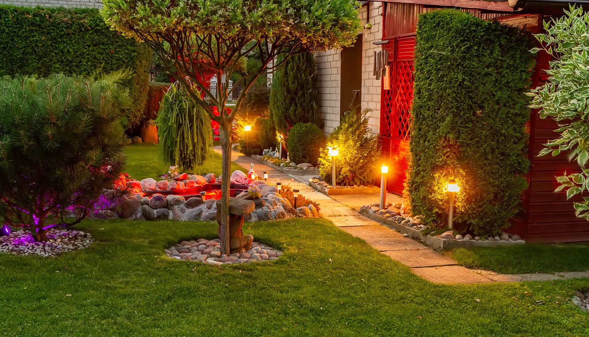 A lush green garden with a path leading to a house at night.