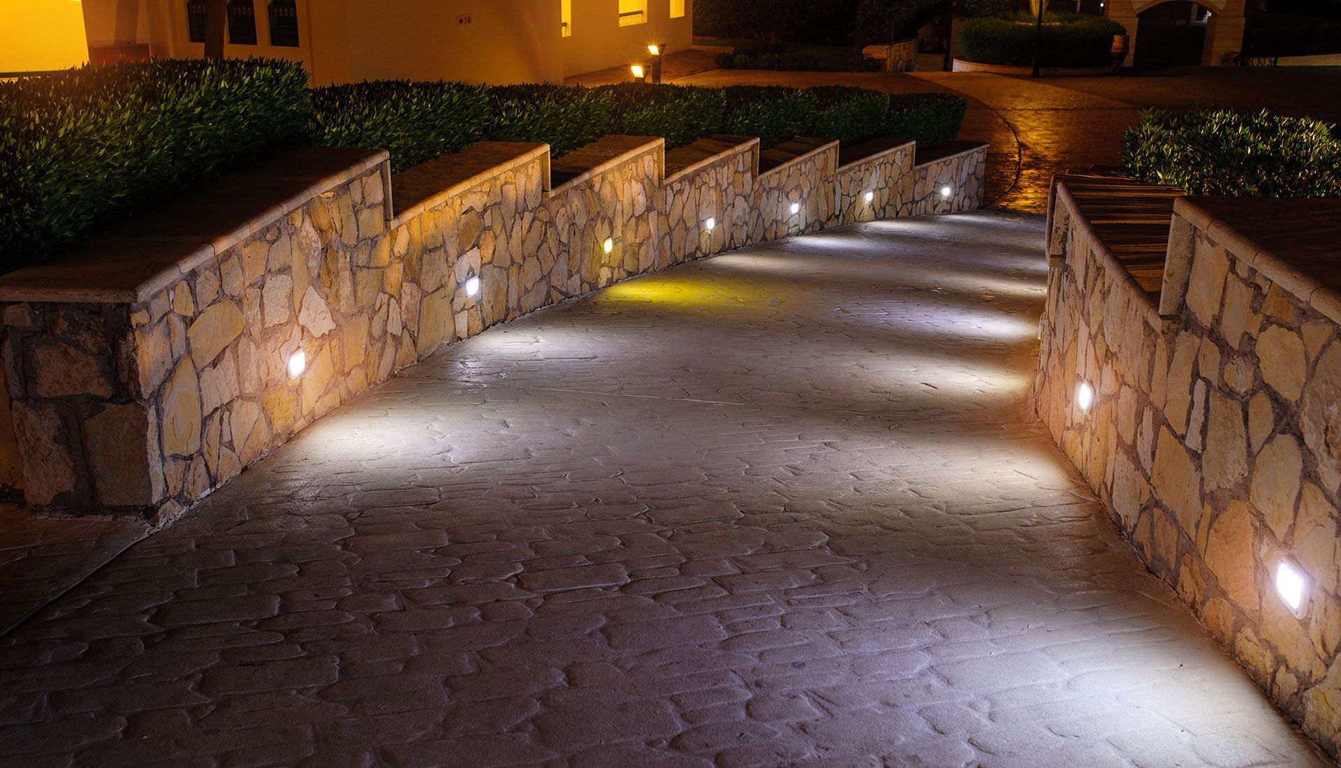 A stone walkway with lights on the side of it at night.