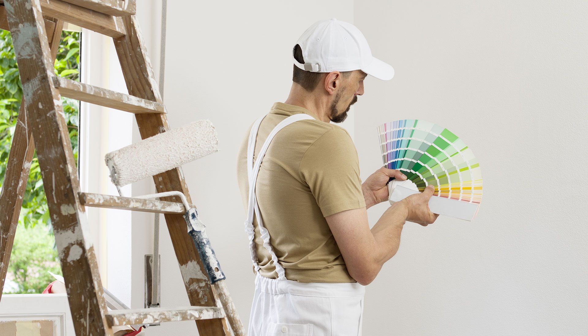 A man is standing next to a ladder holding a palette of paint.