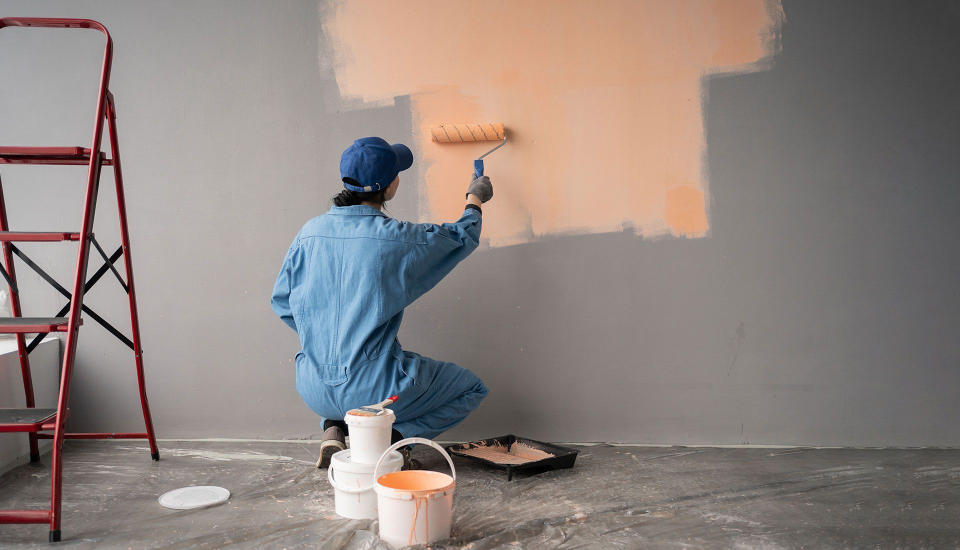 A man is kneeling down and painting a wall with a roller.