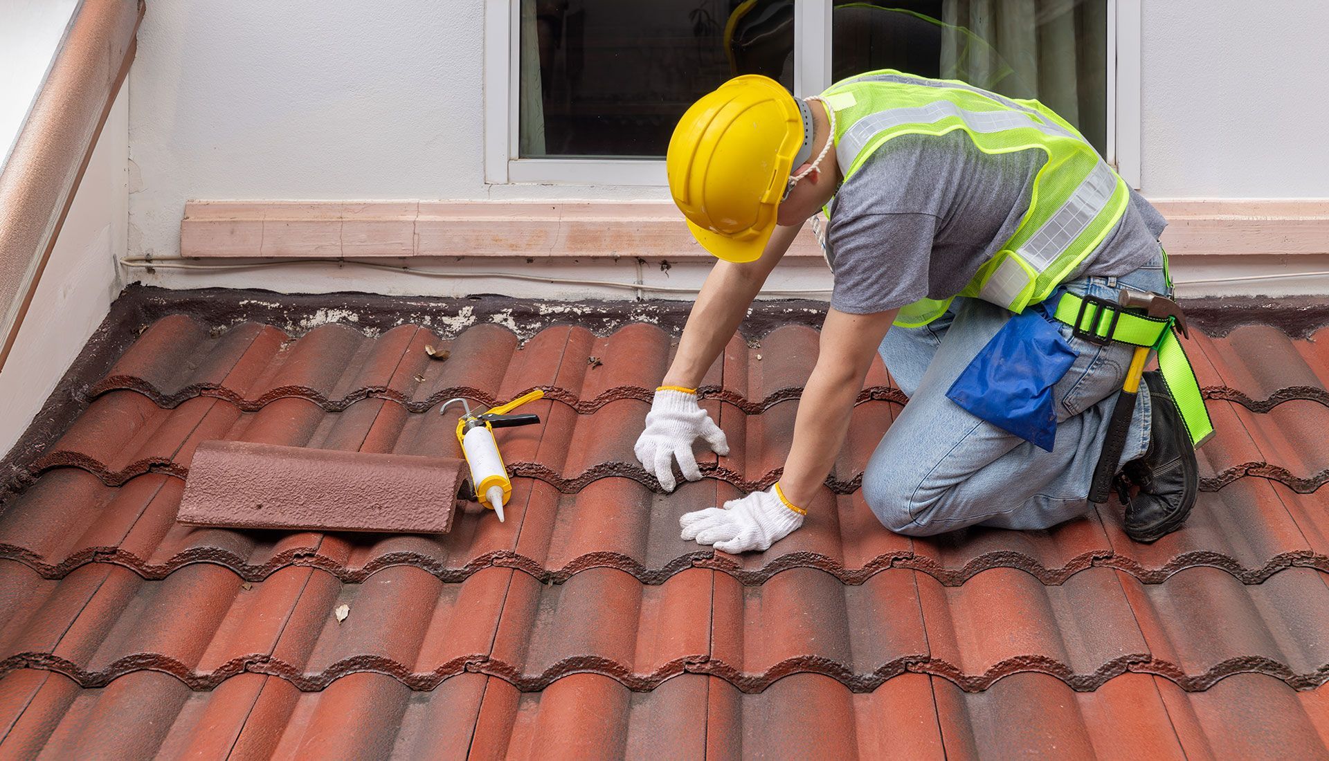 A construction worker is kneeling on a tiled roof.