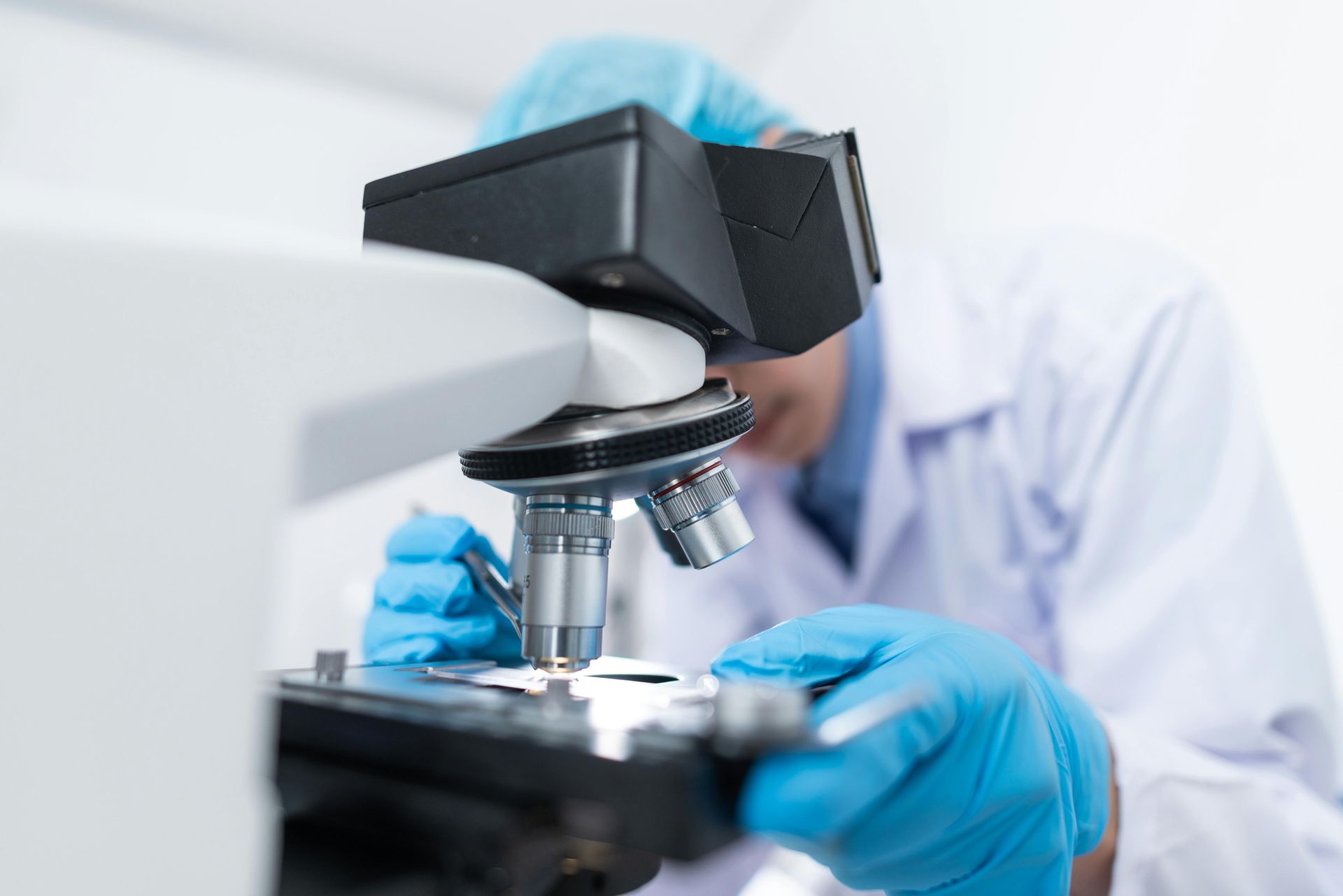 Scientist in lab coat and gloves looking through a microscope.