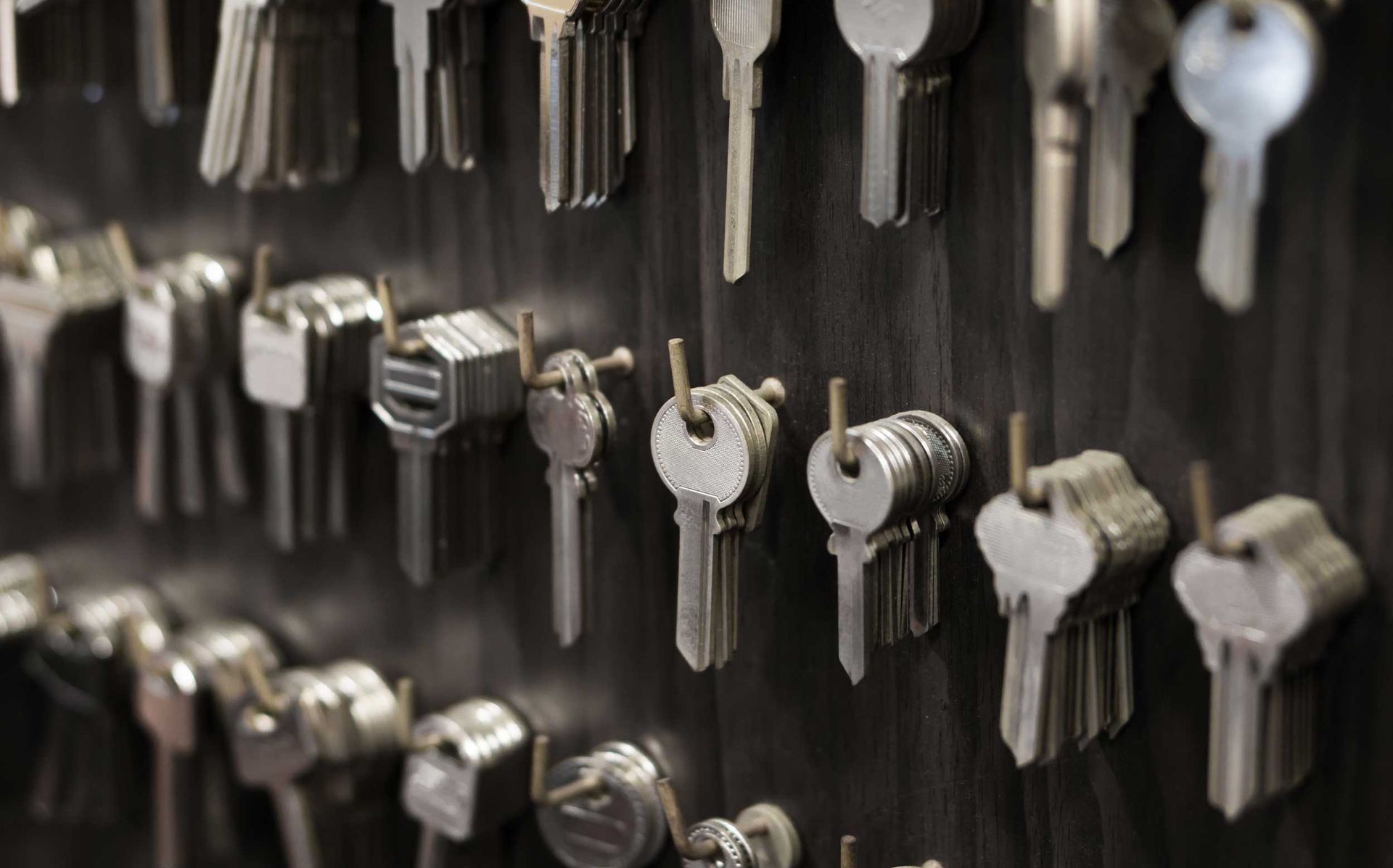 Rows of metal keys hanging on a wall display, organized by size and shape in a locksmith shop.
