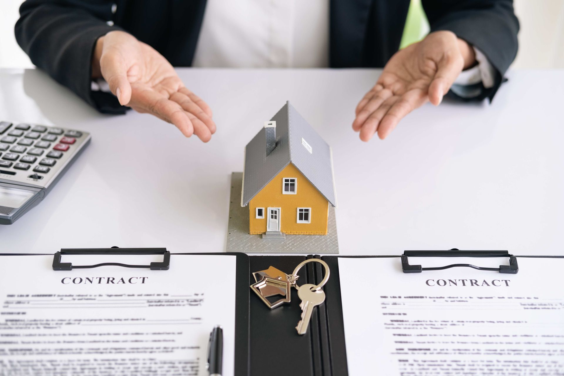 a man is sitting at a desk with a model house and keys
