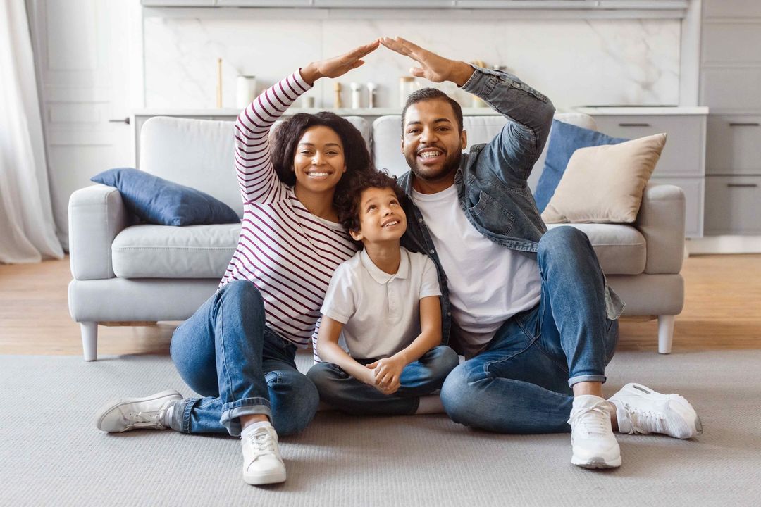 a family is sitting on the floor in front of a couch making a house with their hands