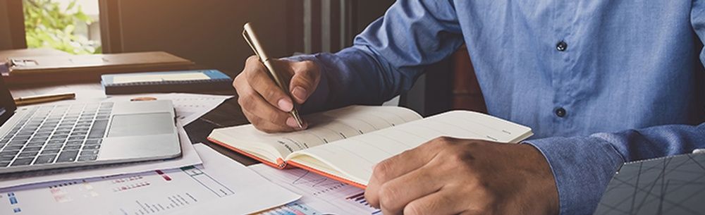 a man is sitting at a desk writing in a notebook
