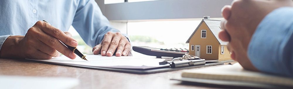 a man is signing a document next to a model house on a clipboard