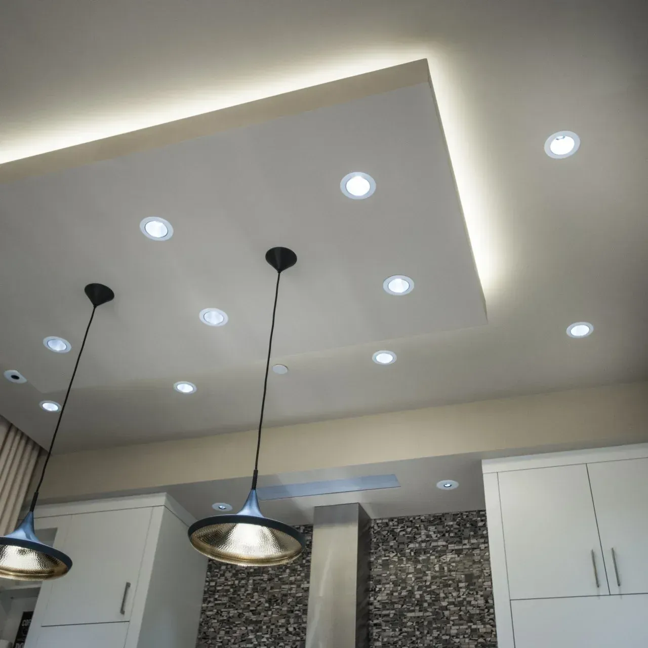 Kitchen ceiling with recessed lights, pendant lights, and indirect lighting around a recessed panel.
