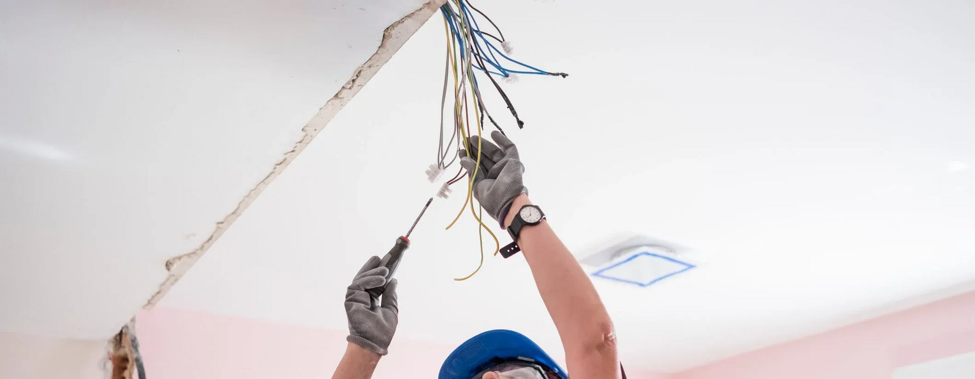 Electrician working on exposed wires in a ceiling with a screwdriver.