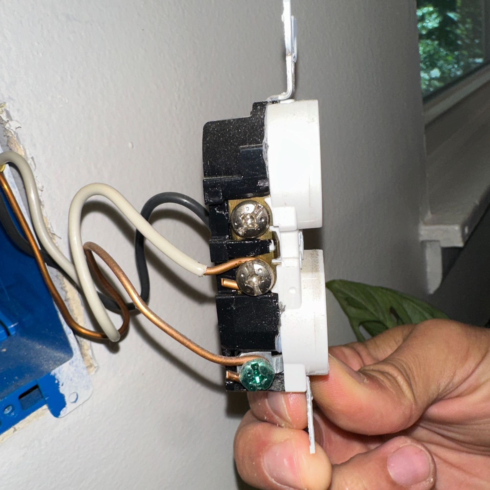 Electrical outlet with wires connected, being held. White, black, copper, and green wires visible.