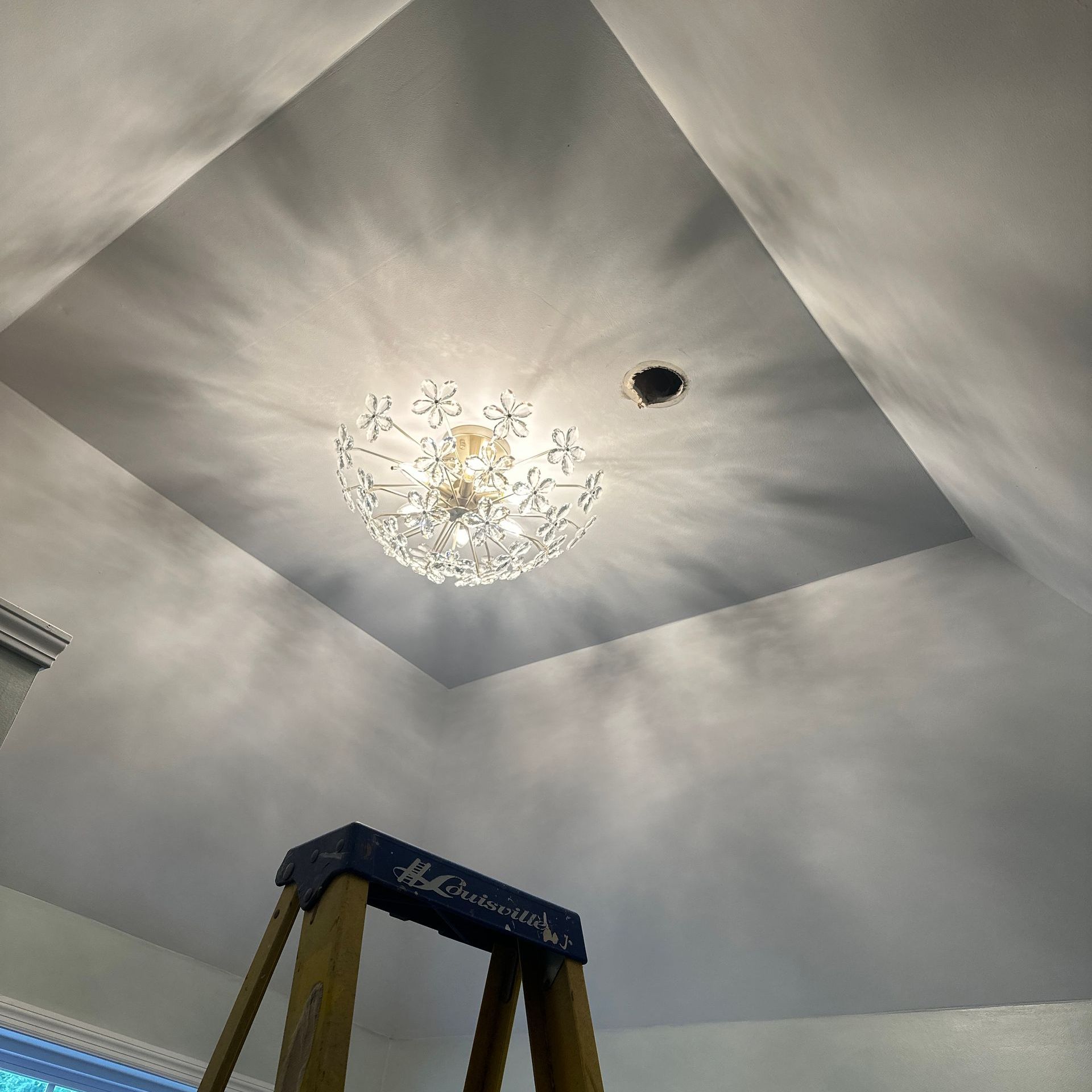 A ladder is sitting under a chandelier in a room.