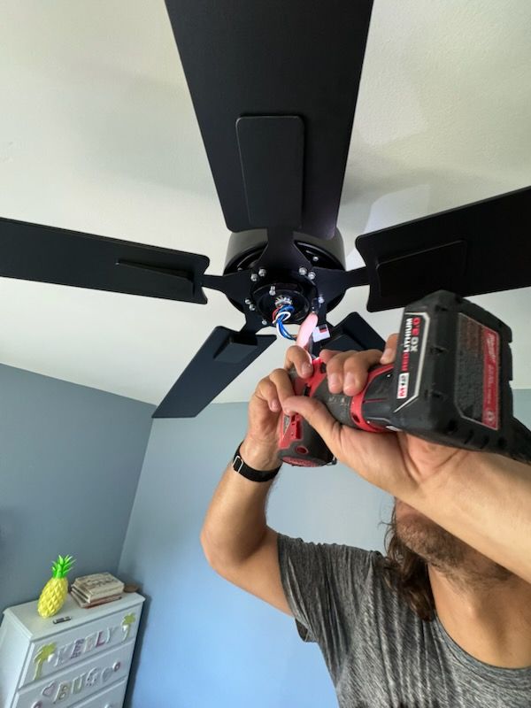 A person is fixing a ceiling fan with a drill.