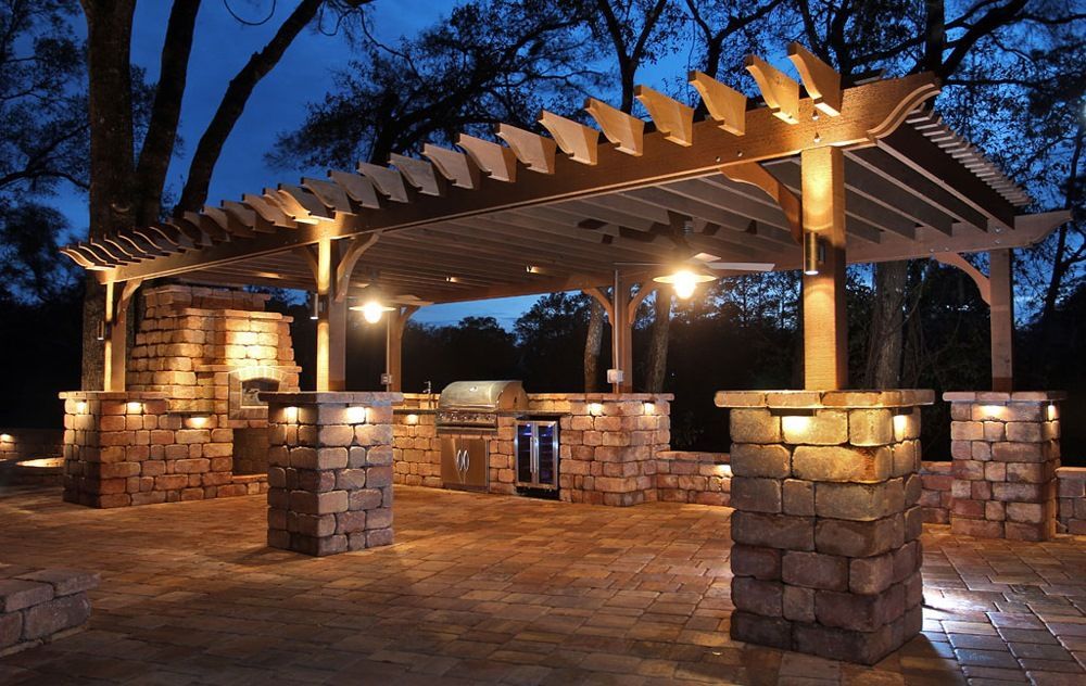 A patio area with a pergola and brick pillars at night