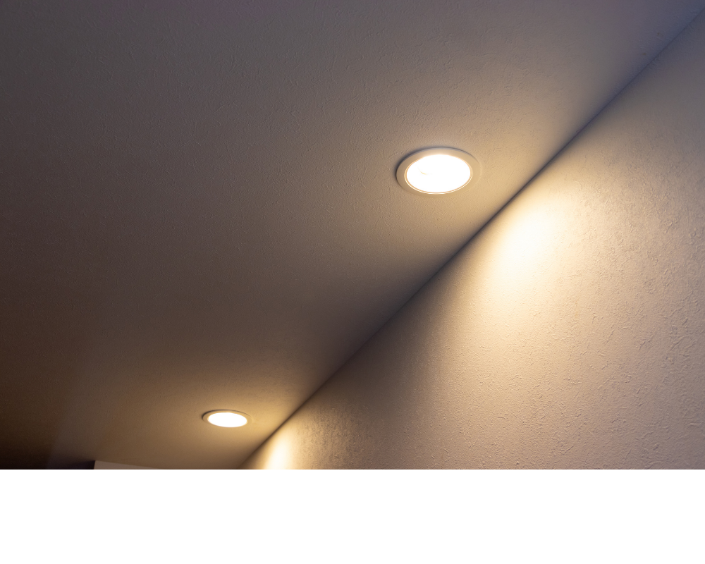 Ceiling corner with two recessed lights casting warm light on a beige wall and ceiling.