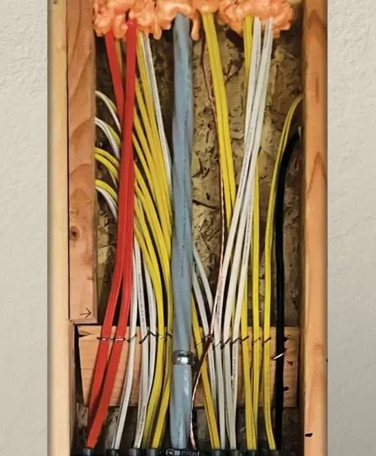 Electrical wires, various colors, run through a wall. Foam seals the top, wooden frame visible.