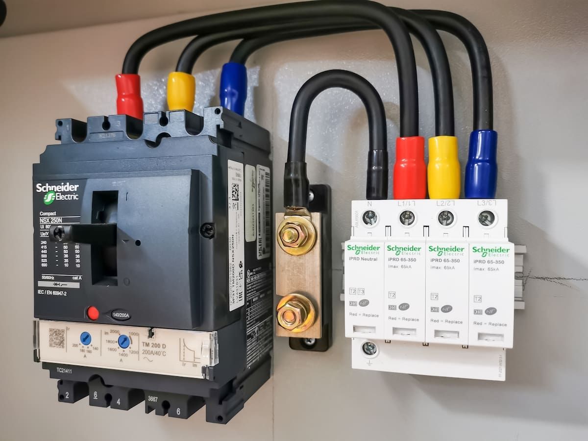 Schneider Electric circuit breaker and surge protective device mounted on a gray panel, connected by color-coded wiring.