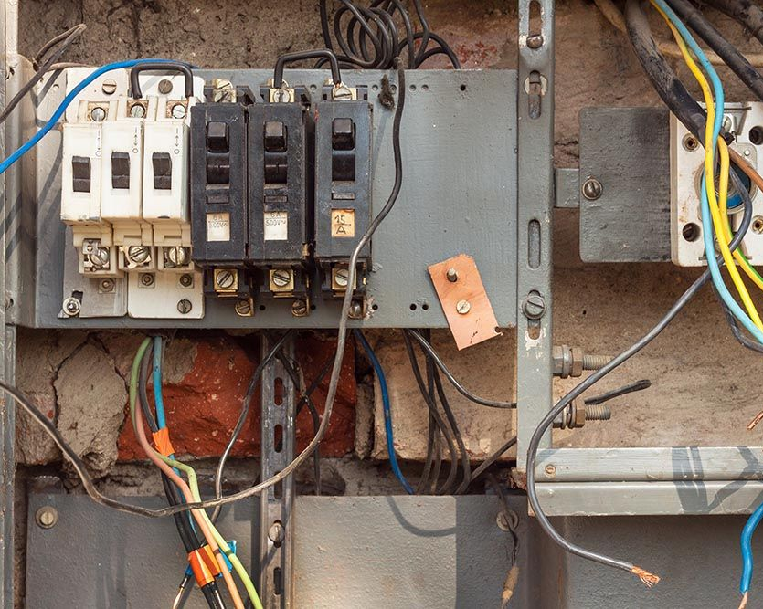Electrical panel with multiple circuit breakers and exposed wiring on a brick wall.