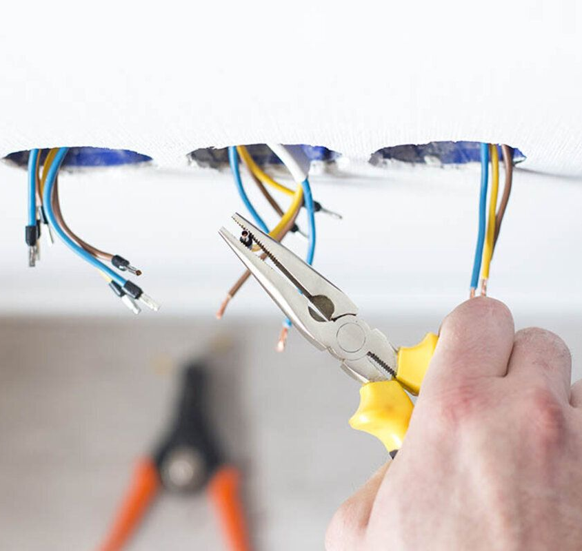 Electrician using pliers on wires protruding from wall.