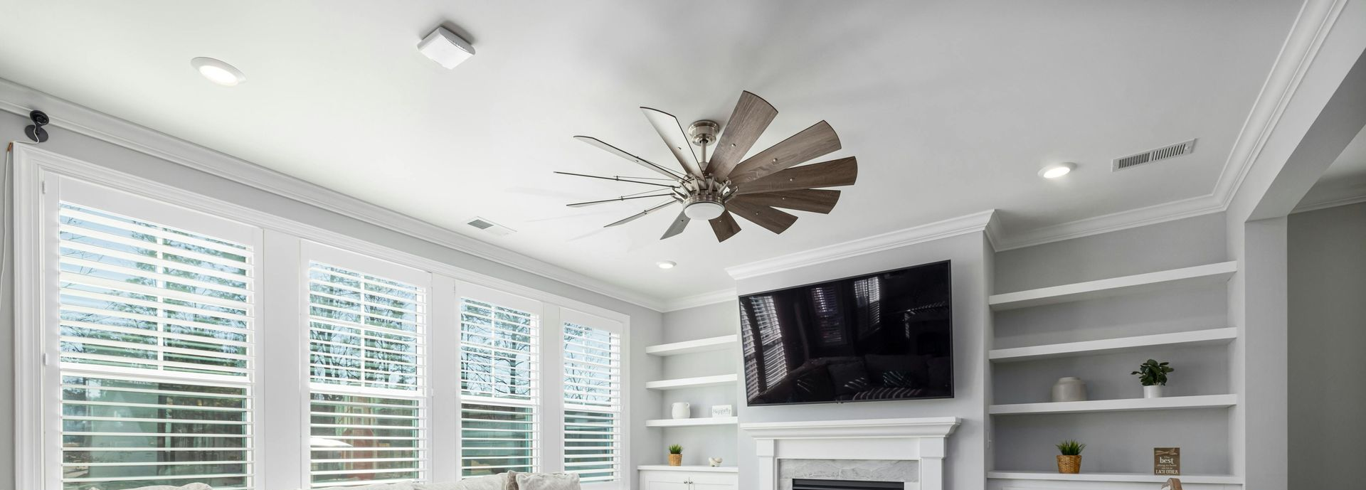 A modern living room with a windmill-style ceiling fan, wall-mounted TV over a fireplace, and built-in shelving.