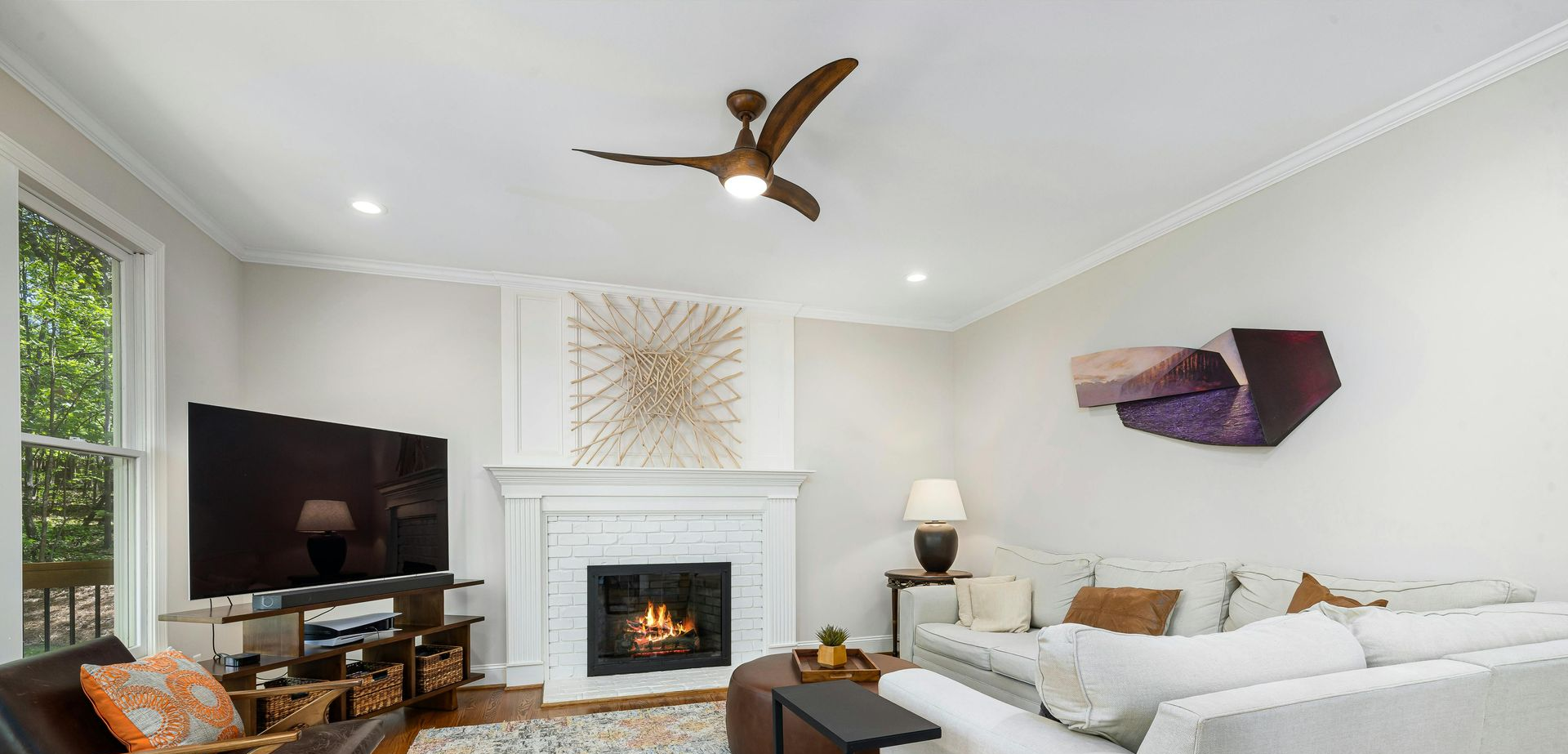 Living room with white walls, fireplace, TV, and ceiling fan. A white couch and artwork are present.