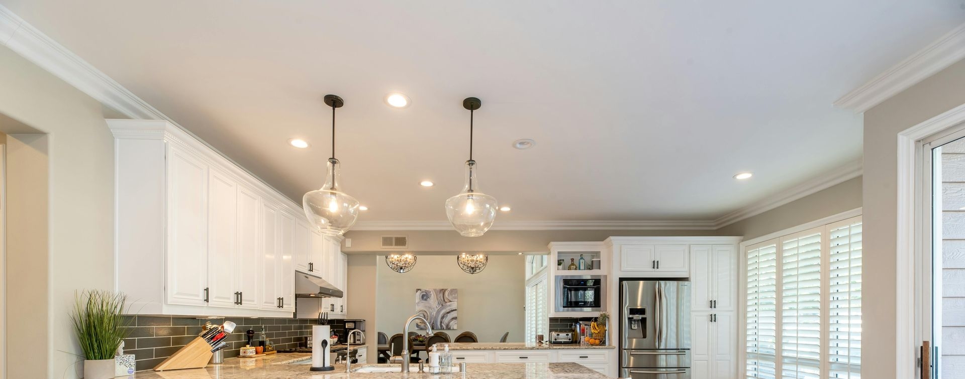 A bright white kitchen with overhead glass pendant lights, stainless steel appliances, and white cabinets.