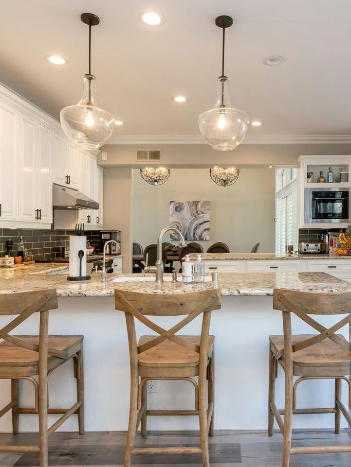 A kitchen with a large island and stools and a sink.