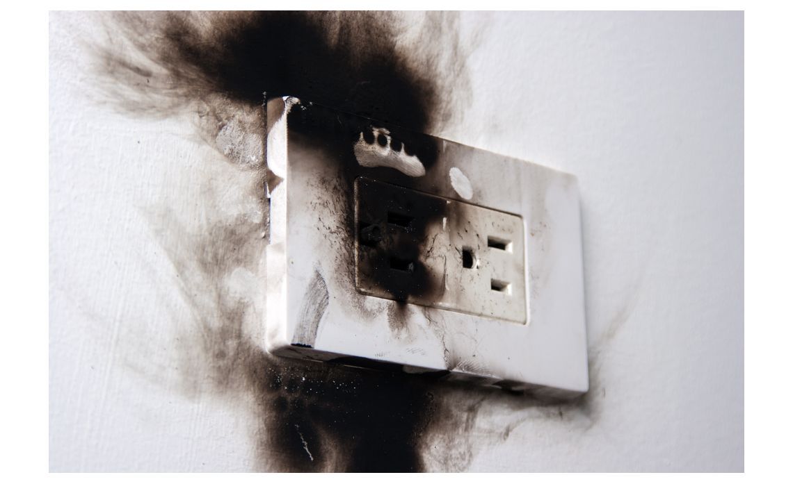 Burnt electrical outlet with black scorch marks on a white wall.