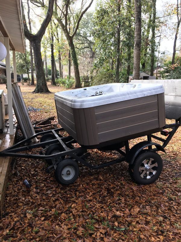 Hot tub on a trailer, brown siding, sitting on dry leaves, outside near a house.