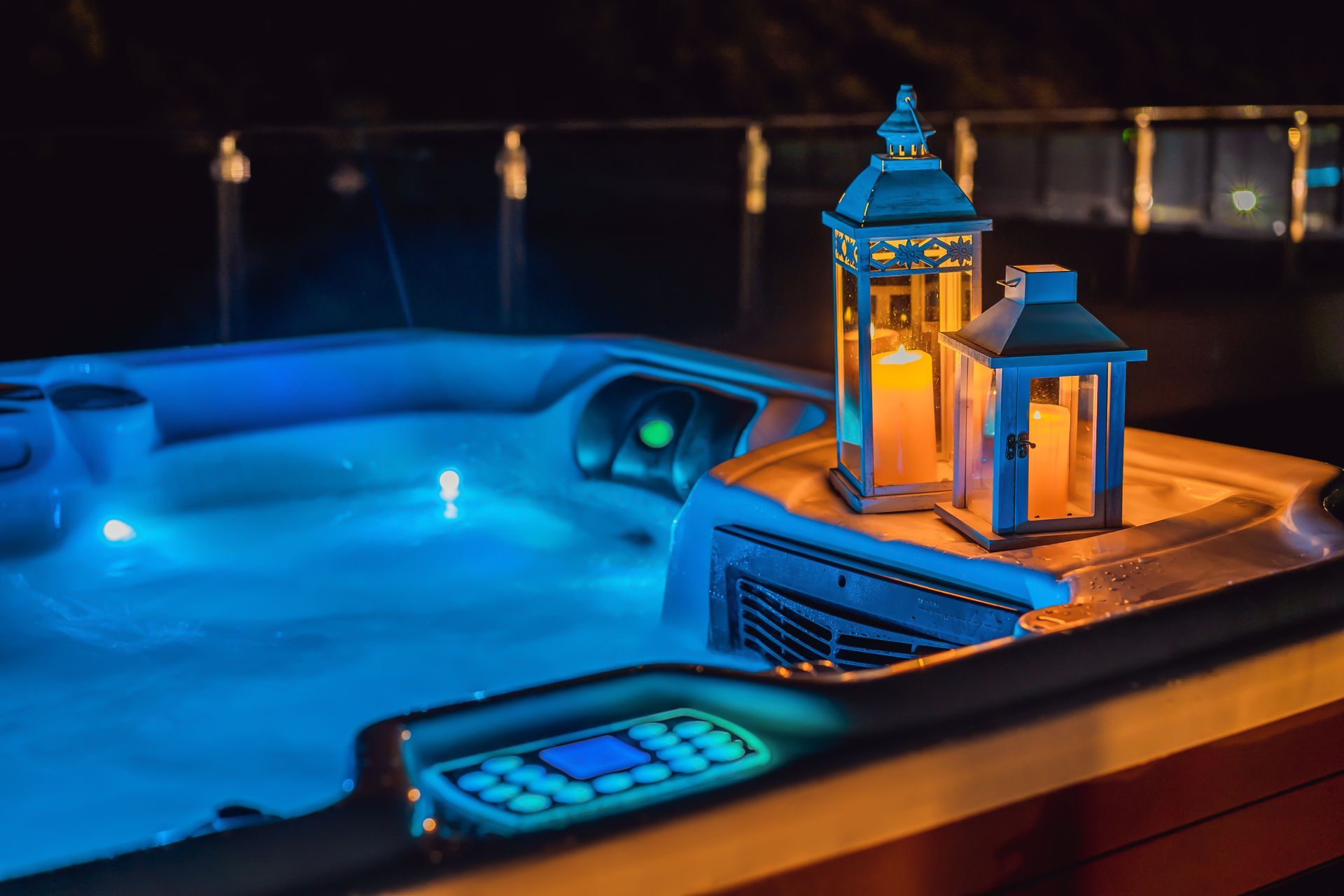 Lit hot tub with blue water, two candle lanterns on the edge. Night setting.