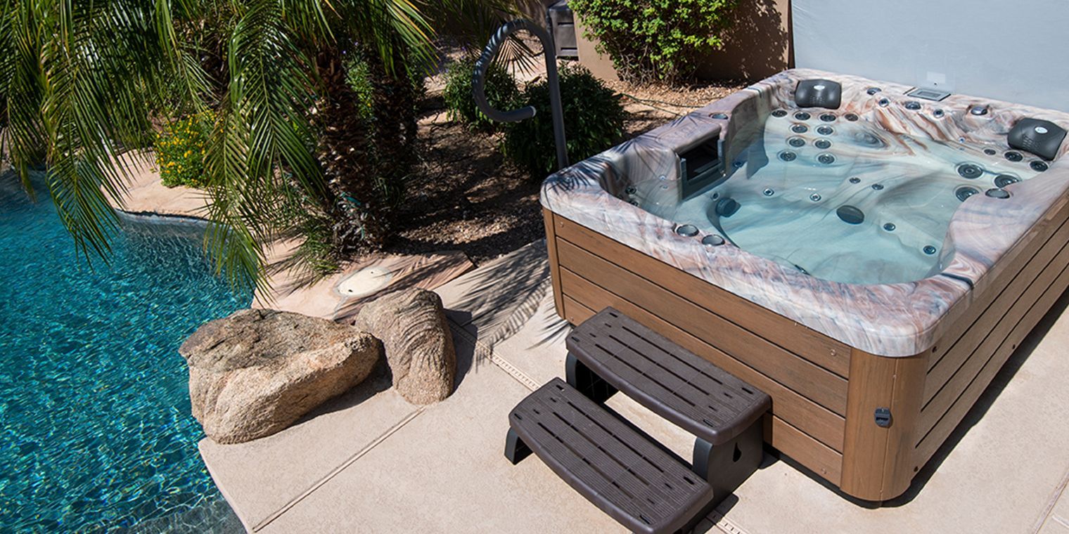 Hot tub next to a pool with steps, palm tree, and rocks.