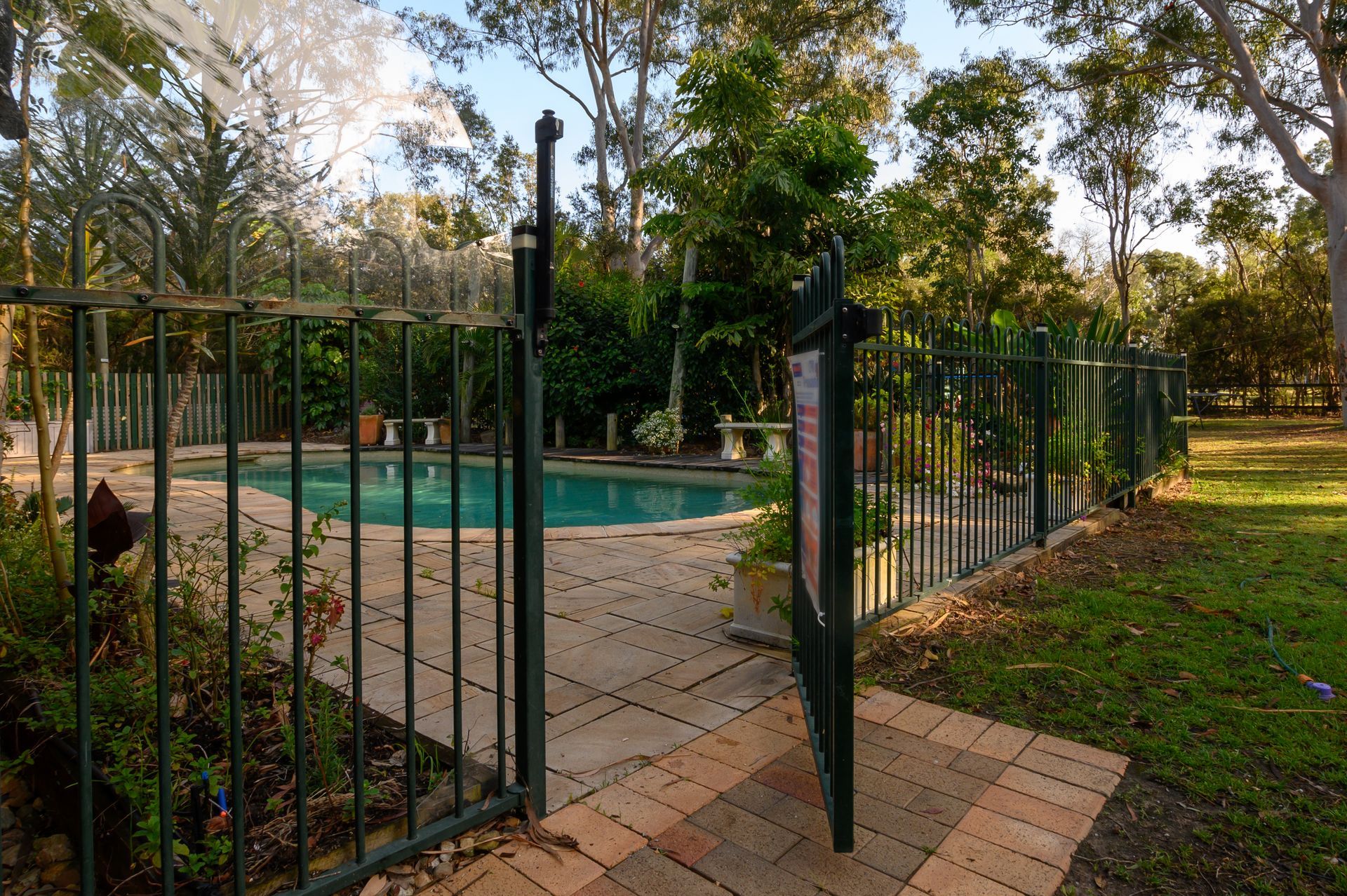 An Open Gate Leads Onto a Stone Patio Surrounding a Swimming Pool — Get My Pool Certified in Palm Beach, QLD