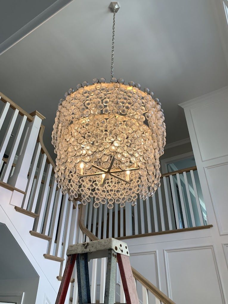 A large chandelier is hanging from the ceiling next to a ladder.