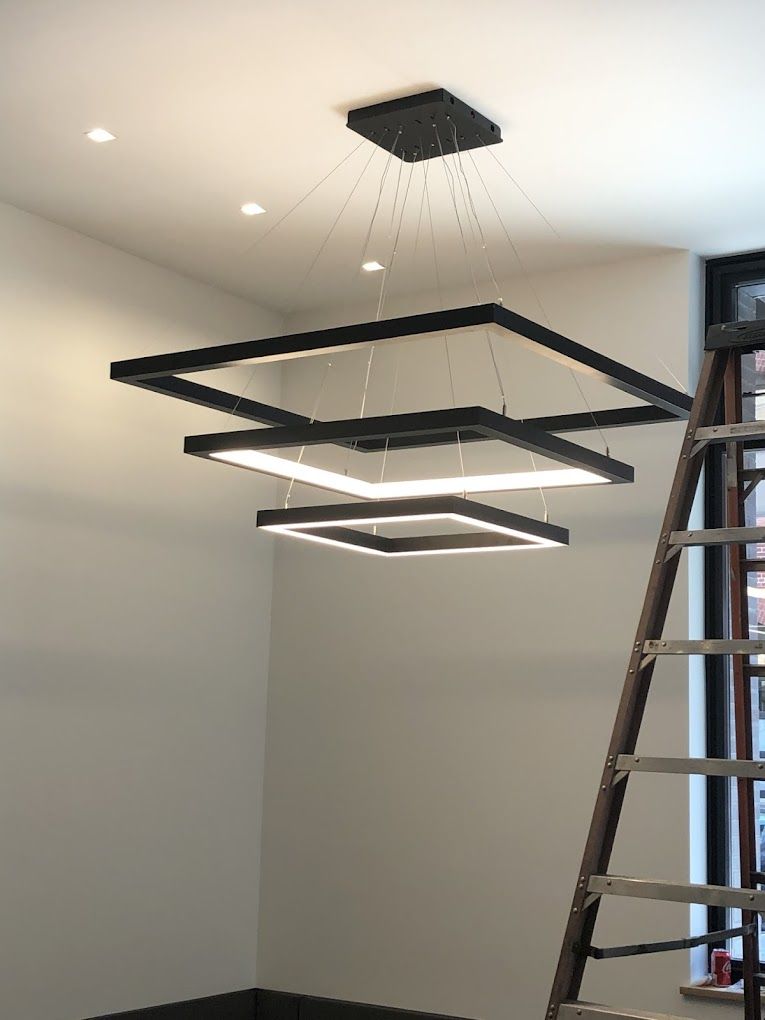 A large square light fixture is hanging from the ceiling in a room with a ladder.