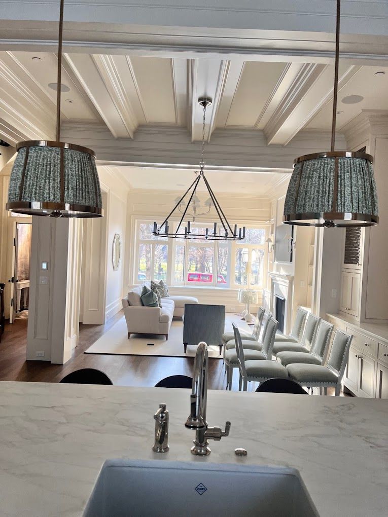 A kitchen with a sink and chairs and a living room in the background