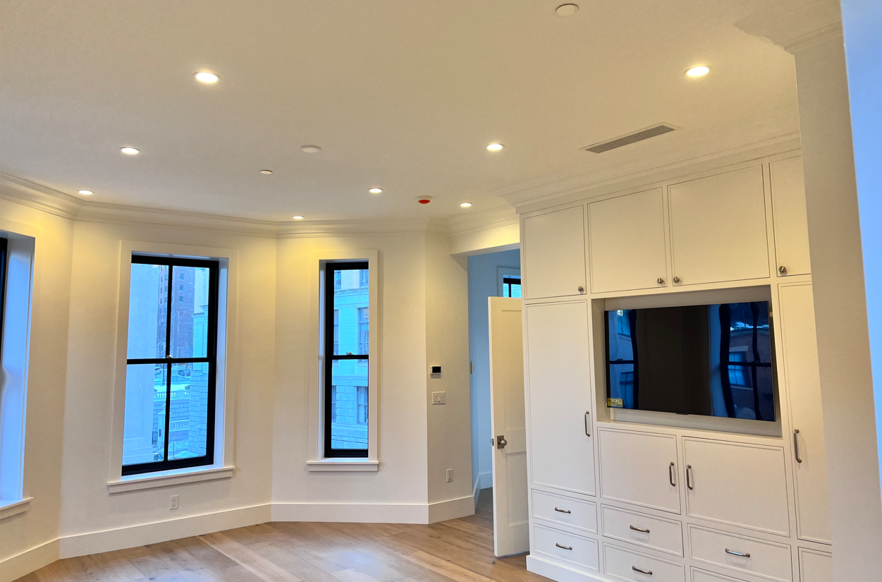 A living room with hardwood floors , white cabinets and a flat screen tv.