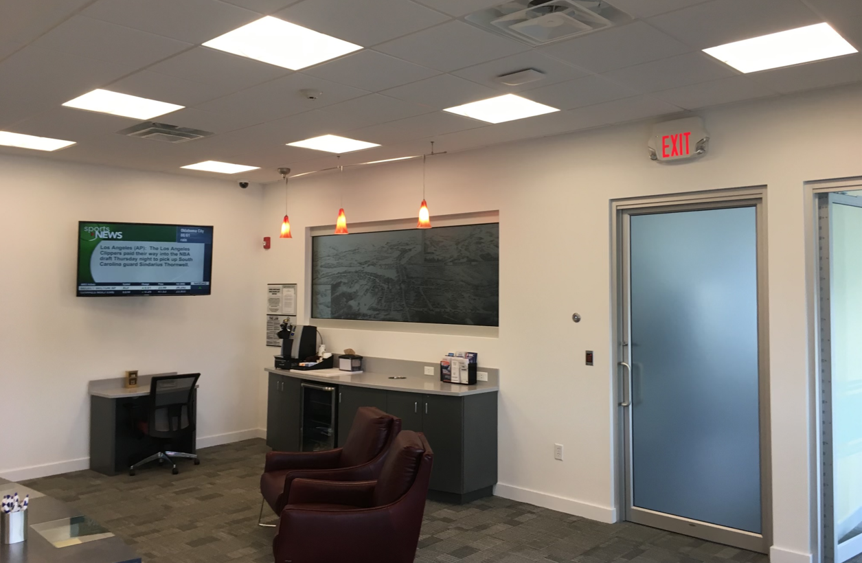 A room with a tv on the wall and a red exit sign.
