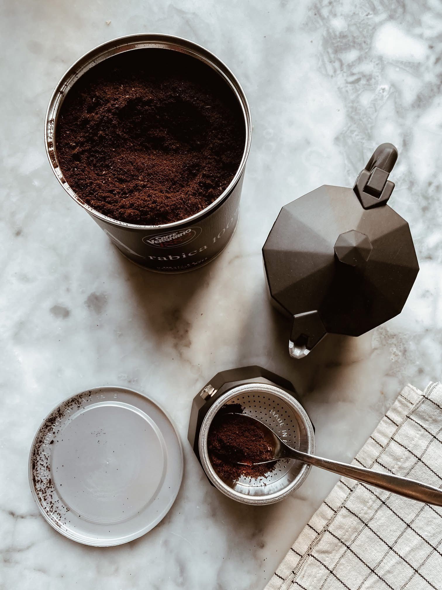 Preparazione del caffè: aprire la lattina di caffè macinato, la moka, il filtro per il caffè con il cucchiaino e uno strofinaccio su una superficie di marmo.